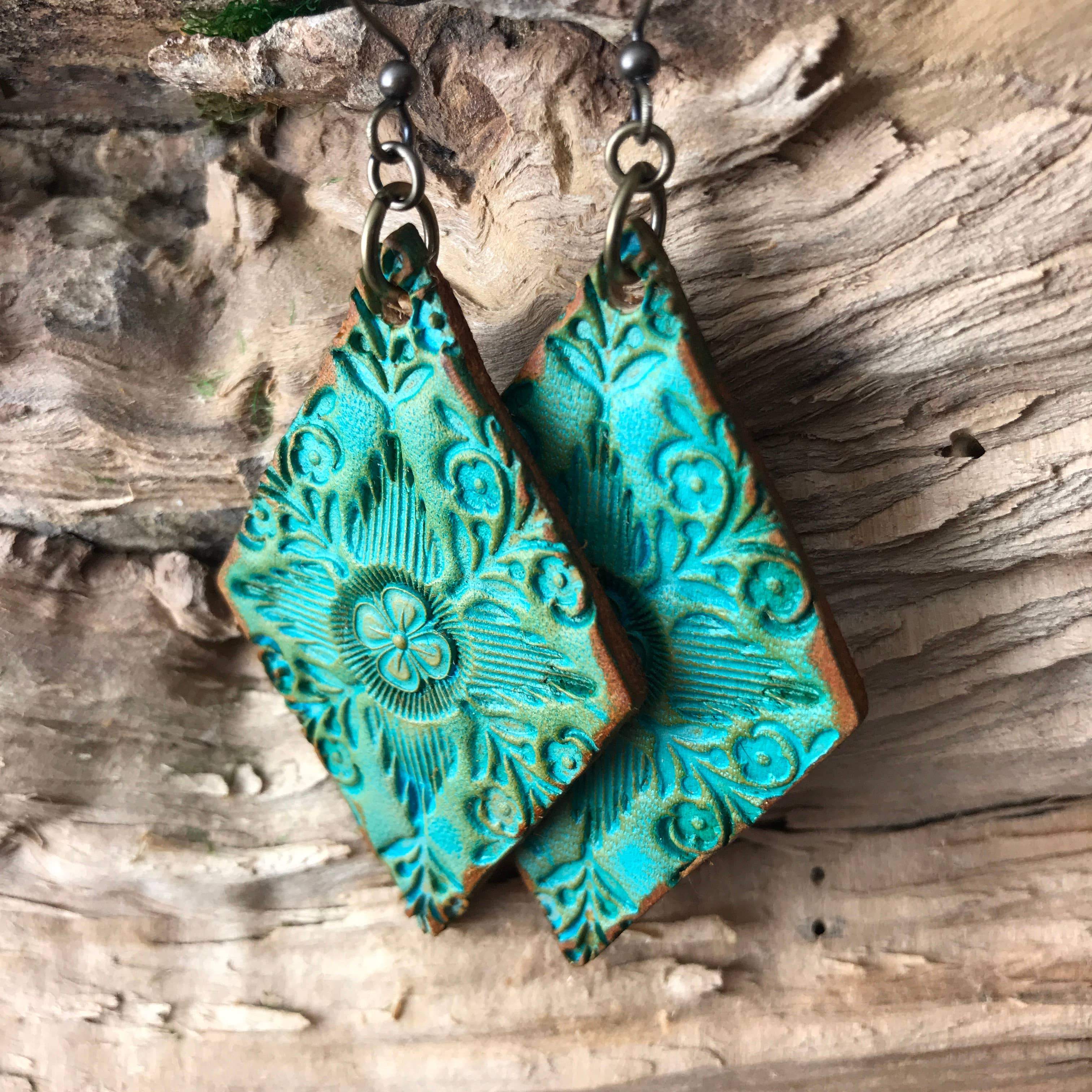 Turquoise Artisan crafted leather embossed earrings on a wooden surface