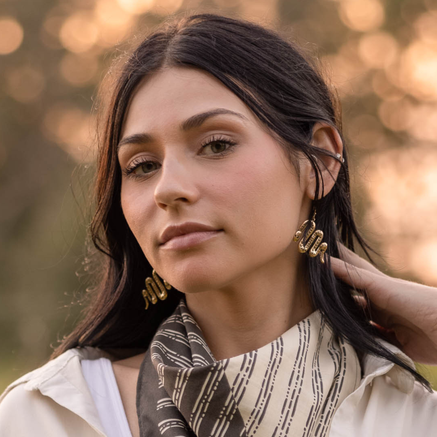 Woman wearing brass snake earrings with a blurred natural background