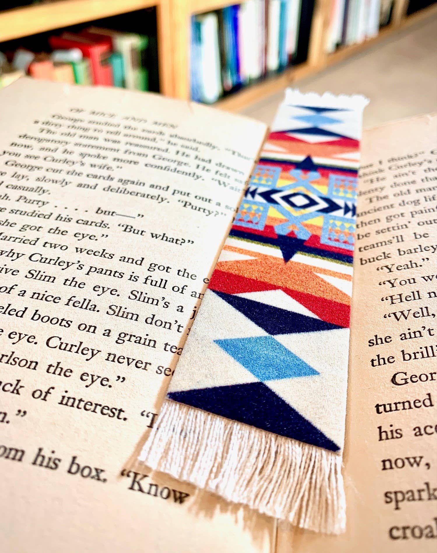 Colorful geometric Pendleton Blanket patterned bookmark on an open book with blurred bookshelf in the background