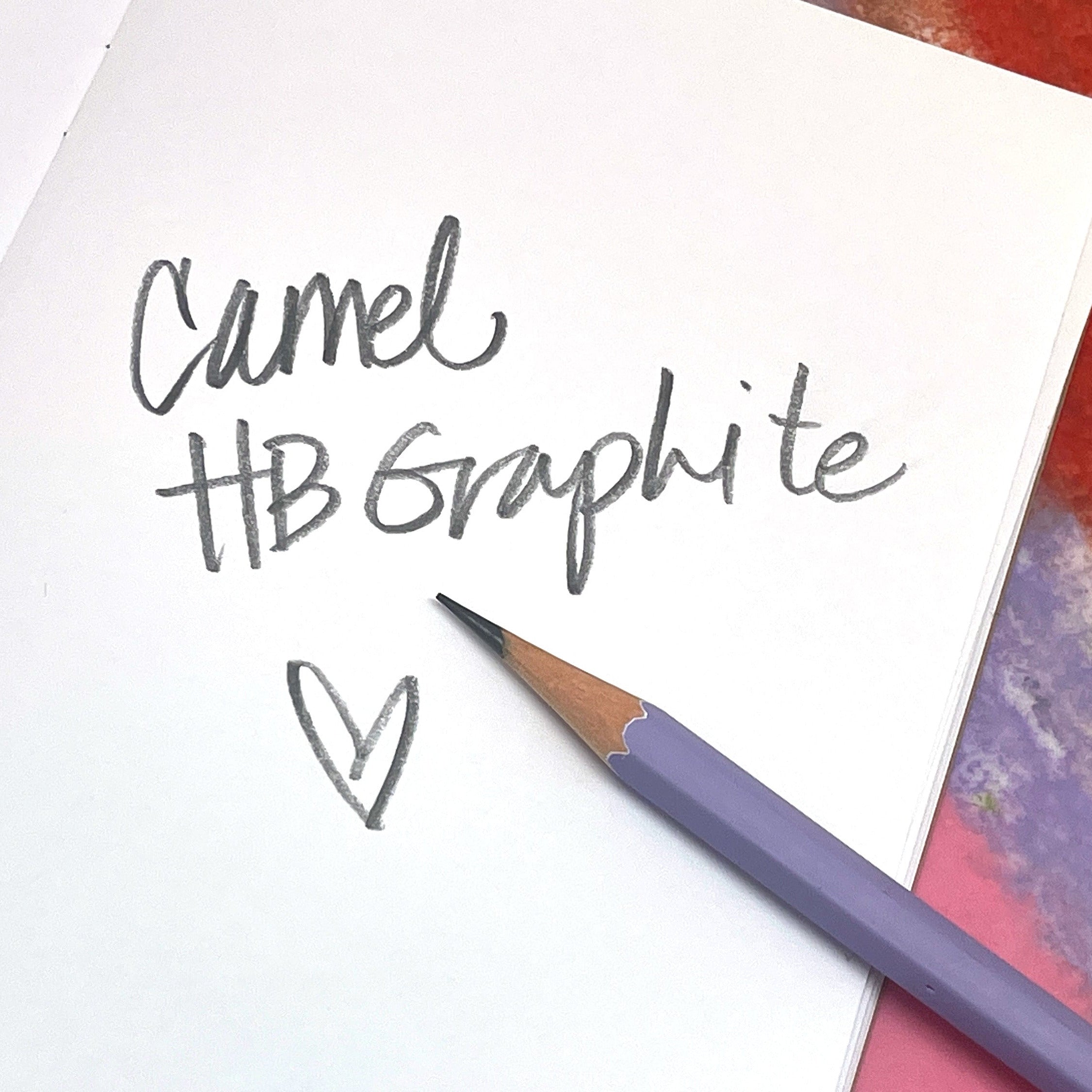 Purple Camel HB graphite pencil on a white sheet of paper with 'Camel HB Graphite' hand writing text and a heart.