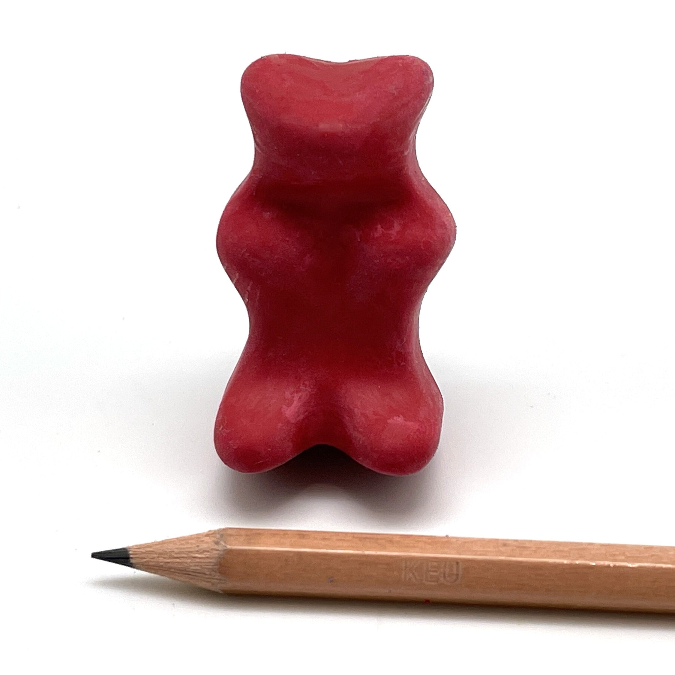 Red gummy bear-shaped eraser with built in pencil sharpener next to a wooden pencil on a white background