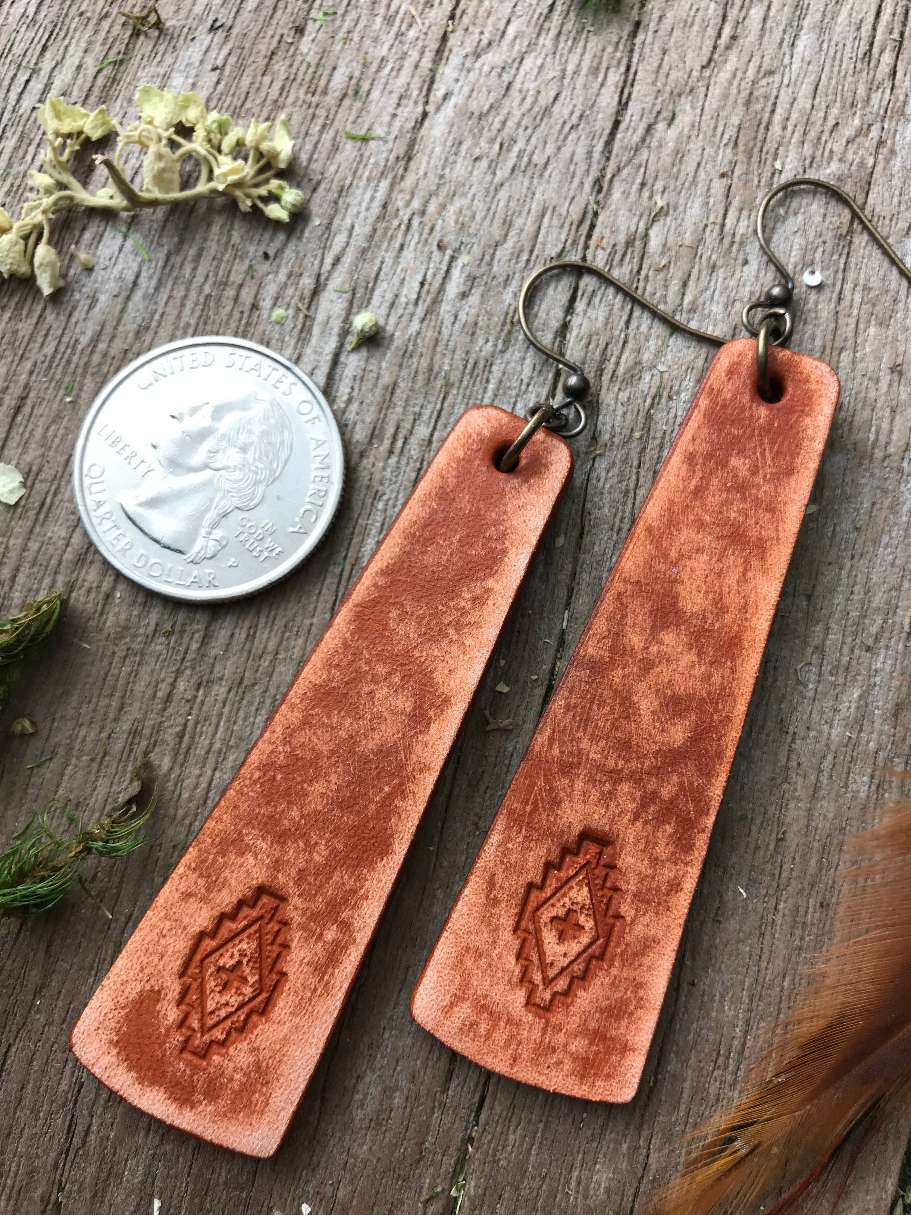 Brown leather earrings on a wooden surface with a coin for scale.