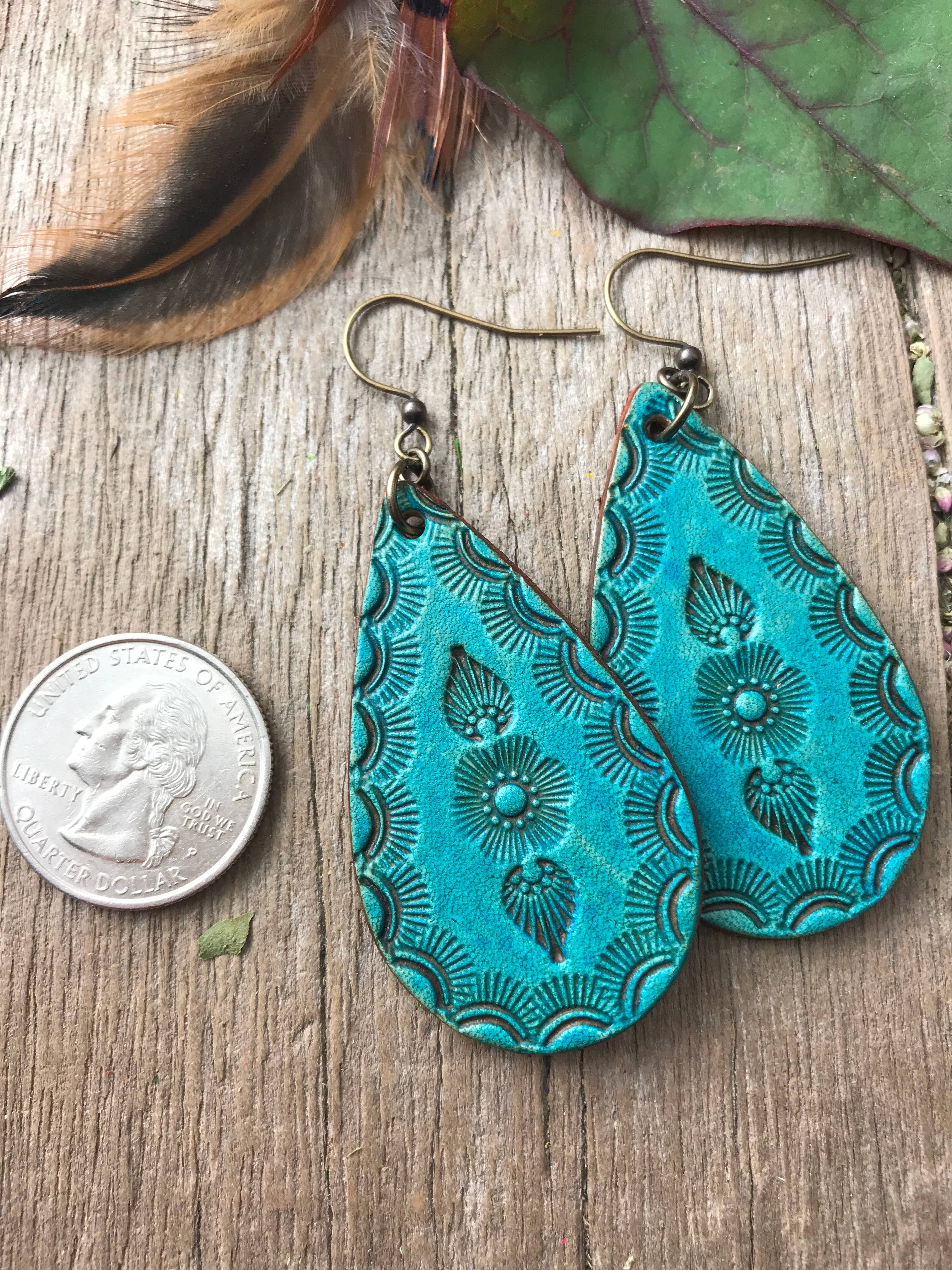 Turquoise patterned earrings on a wooden surface with a quarter for scale.