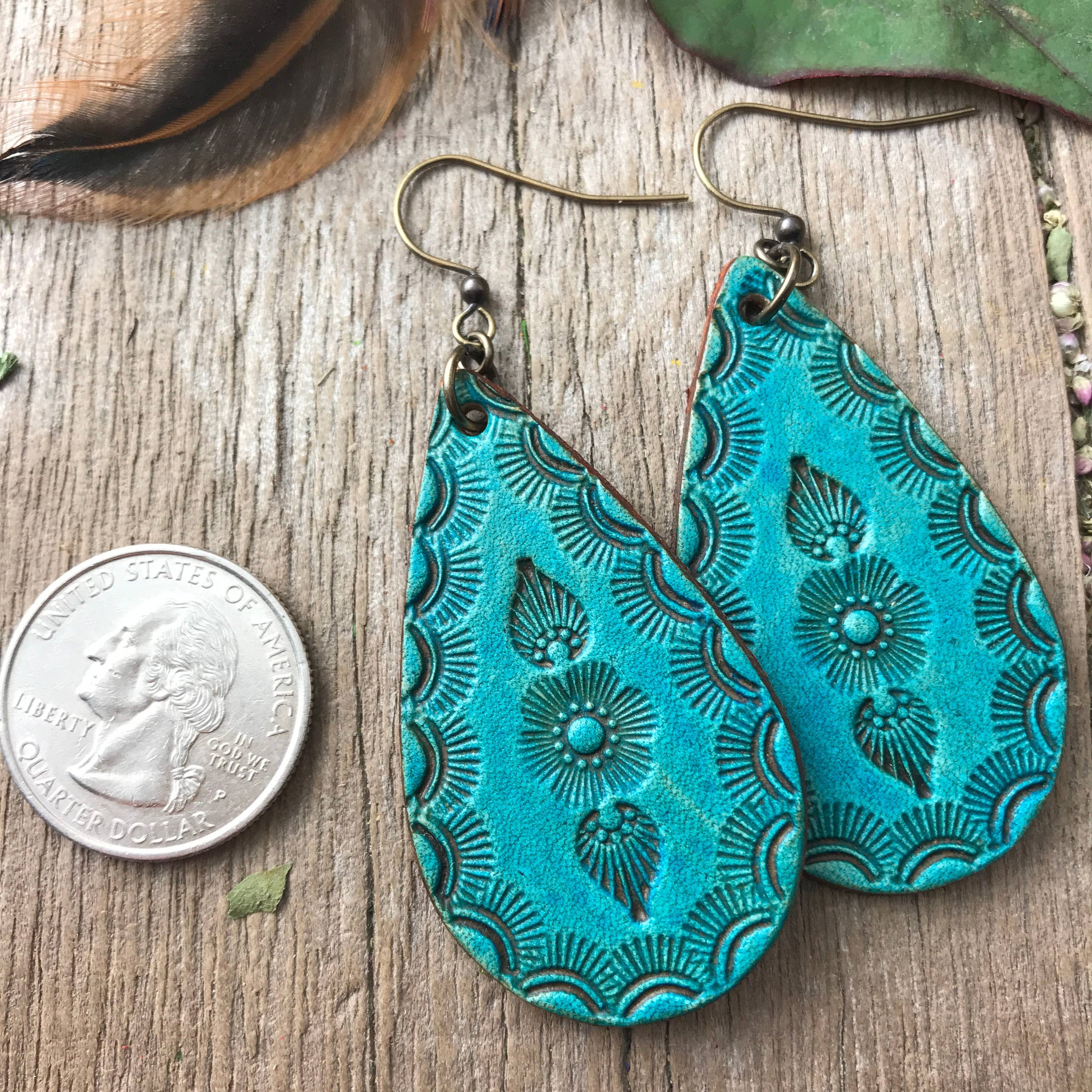 Turquoise patterned earrings on a wooden surface with a quarter for scale.