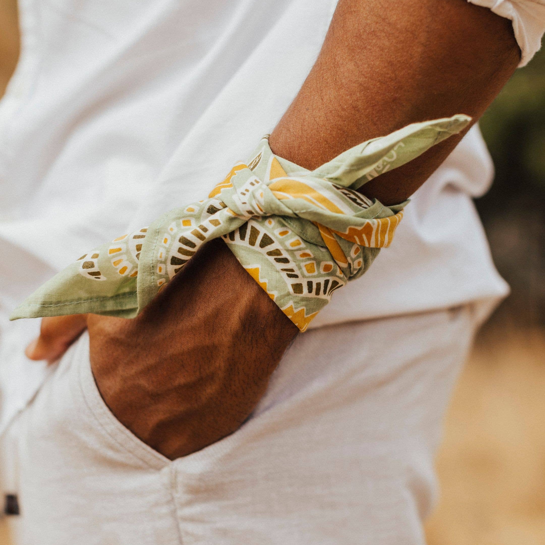 Person wearing a green bandana with yellow patterns on their wrist, against a blurred natural background.
