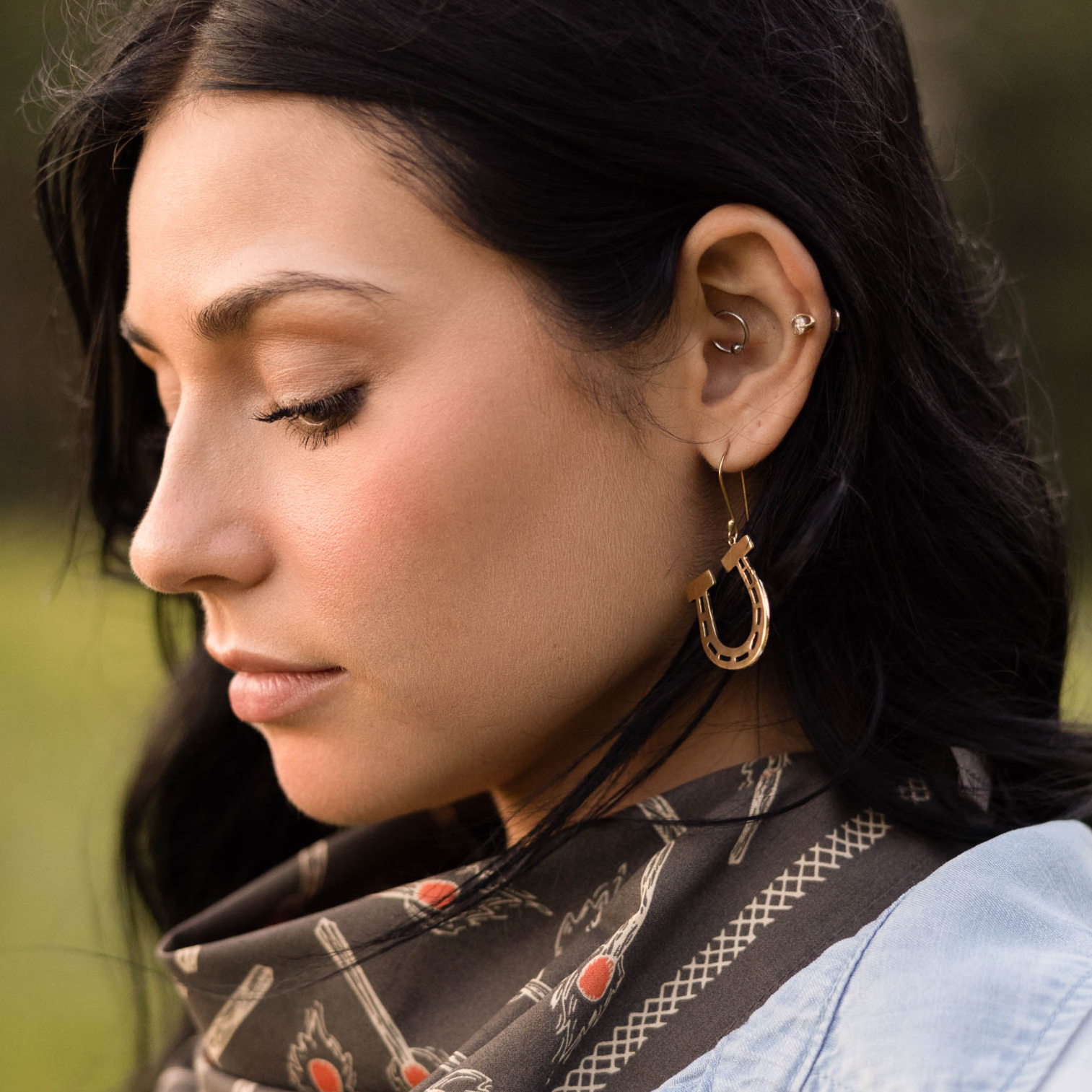 Close-up of a woman wearing horseshoe dangle earrings with a blurred natural background