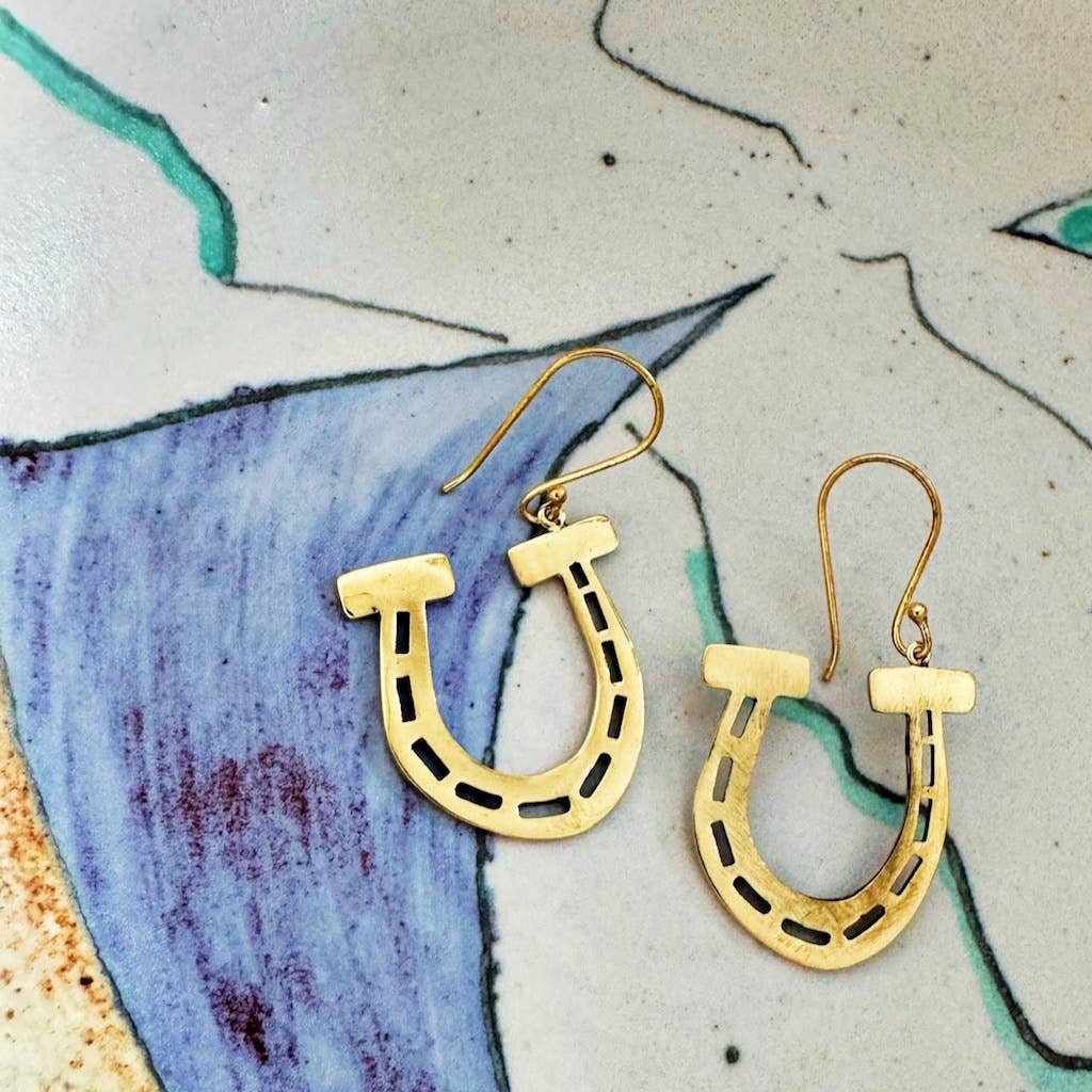 Gold-tone brass horseshoe-shaped earrings on a textured surface with artistic design