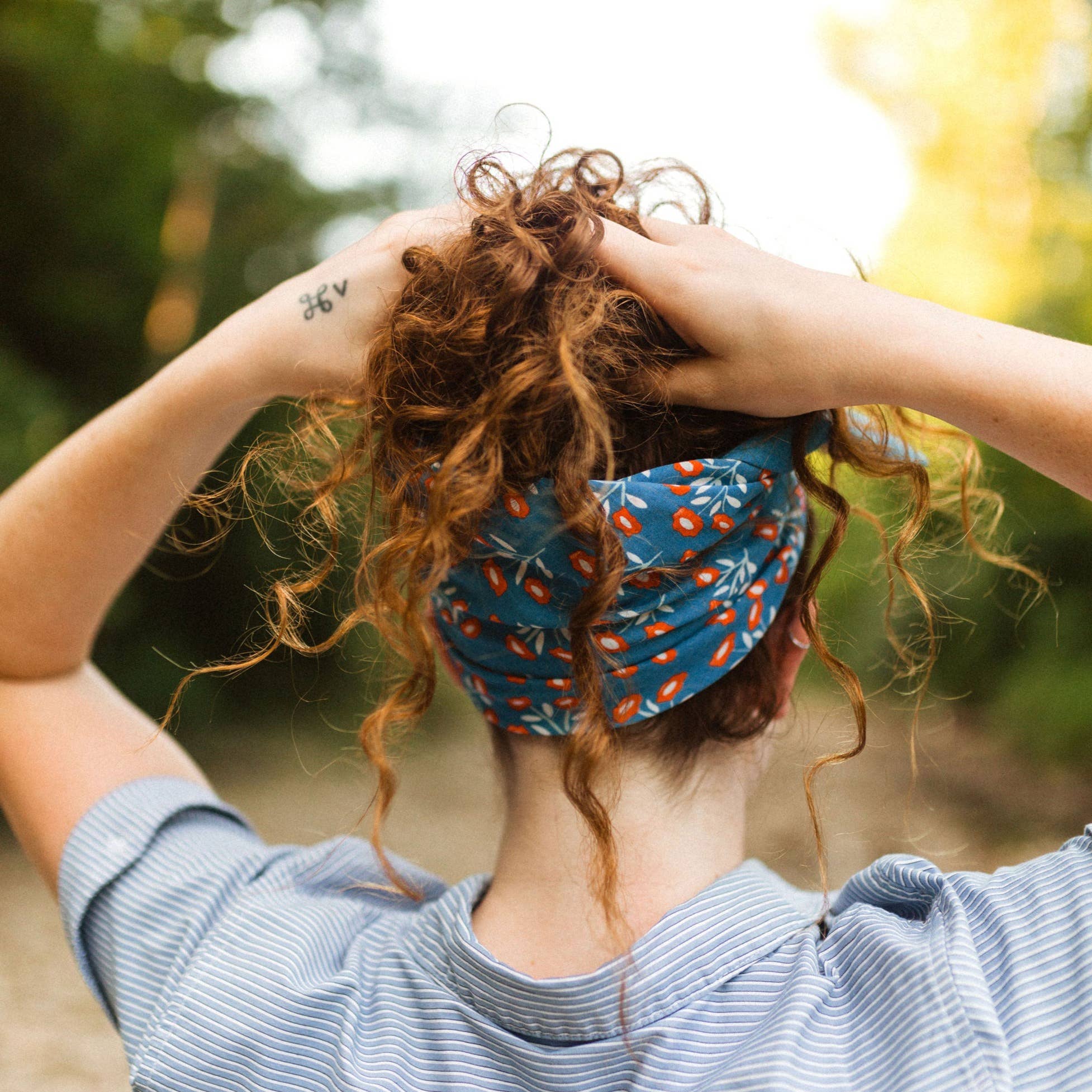 Person with curly hair wearing a blue red and white floral patterns bandana