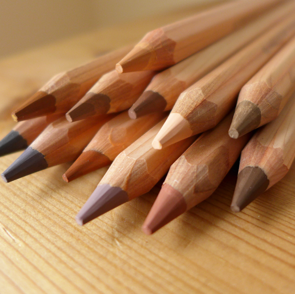 A set of jumbo colored pencils with skin tone colors, displayed on a wooden surface, with natural wood finish and hexagonal shape.