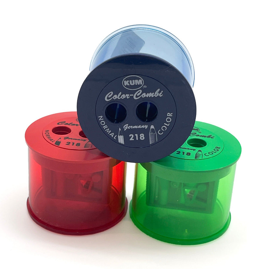 Three translucent plastic pencil sharpener cylinders in red, green, and blue, arranged together on a white background. The top sharpener is dark blue and displays the brand 'KUM' and model 'Color-Combi'.