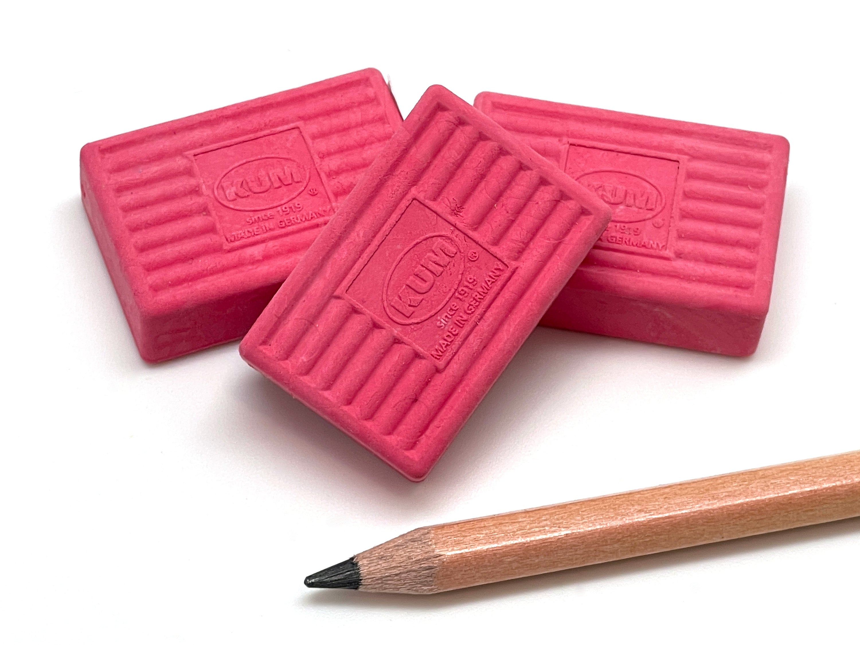 Three pink KUM erasers with a pencil on a white background
