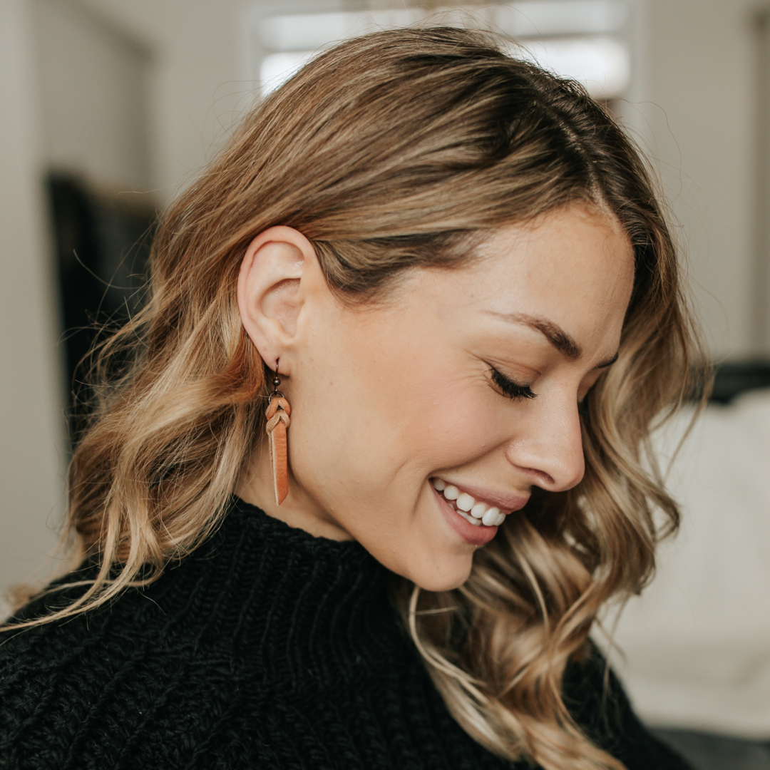 Woman wearing braided leather earrings, smiling indoors.