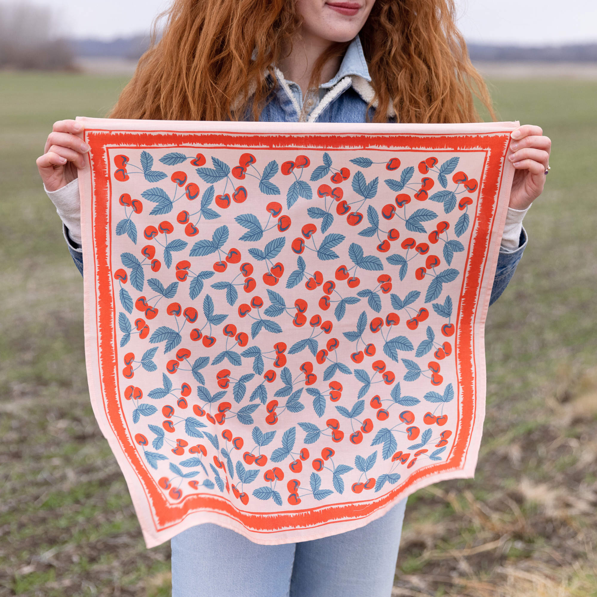 Lady holding a cherry patterned bandana with red and blue designs in an outdoor setting