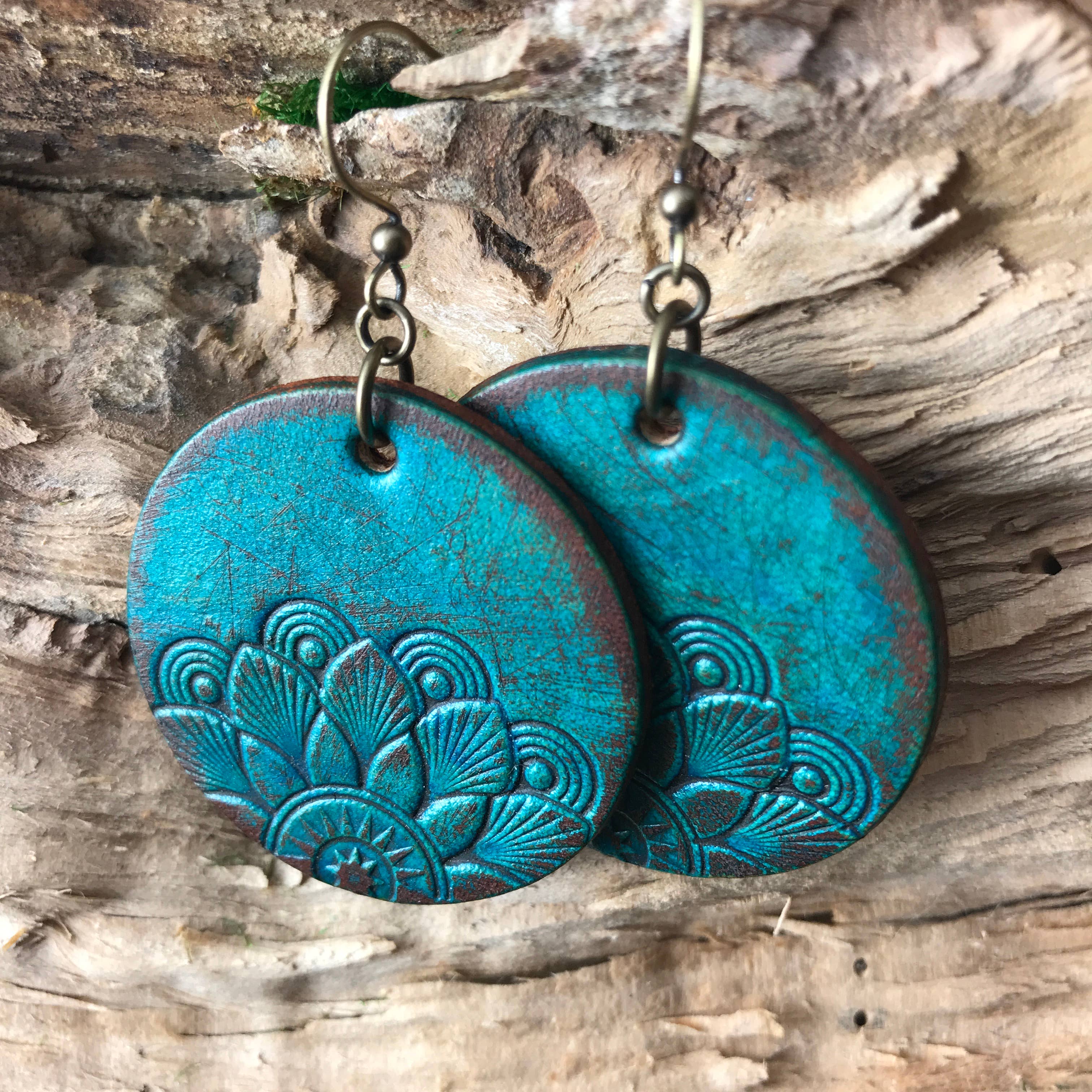 Pair of blue hand tooled leather earrings with mandala pattern on a wooden surface