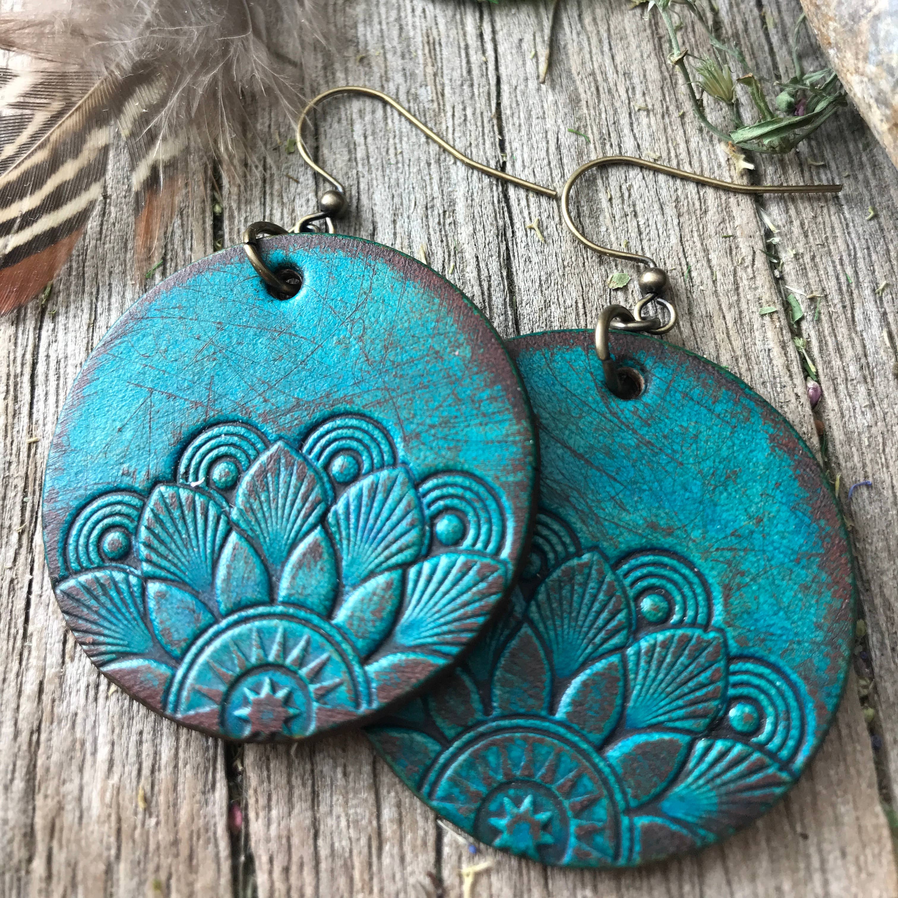Turquoise mandala earrings on a wooden surface with feathers and flowers.