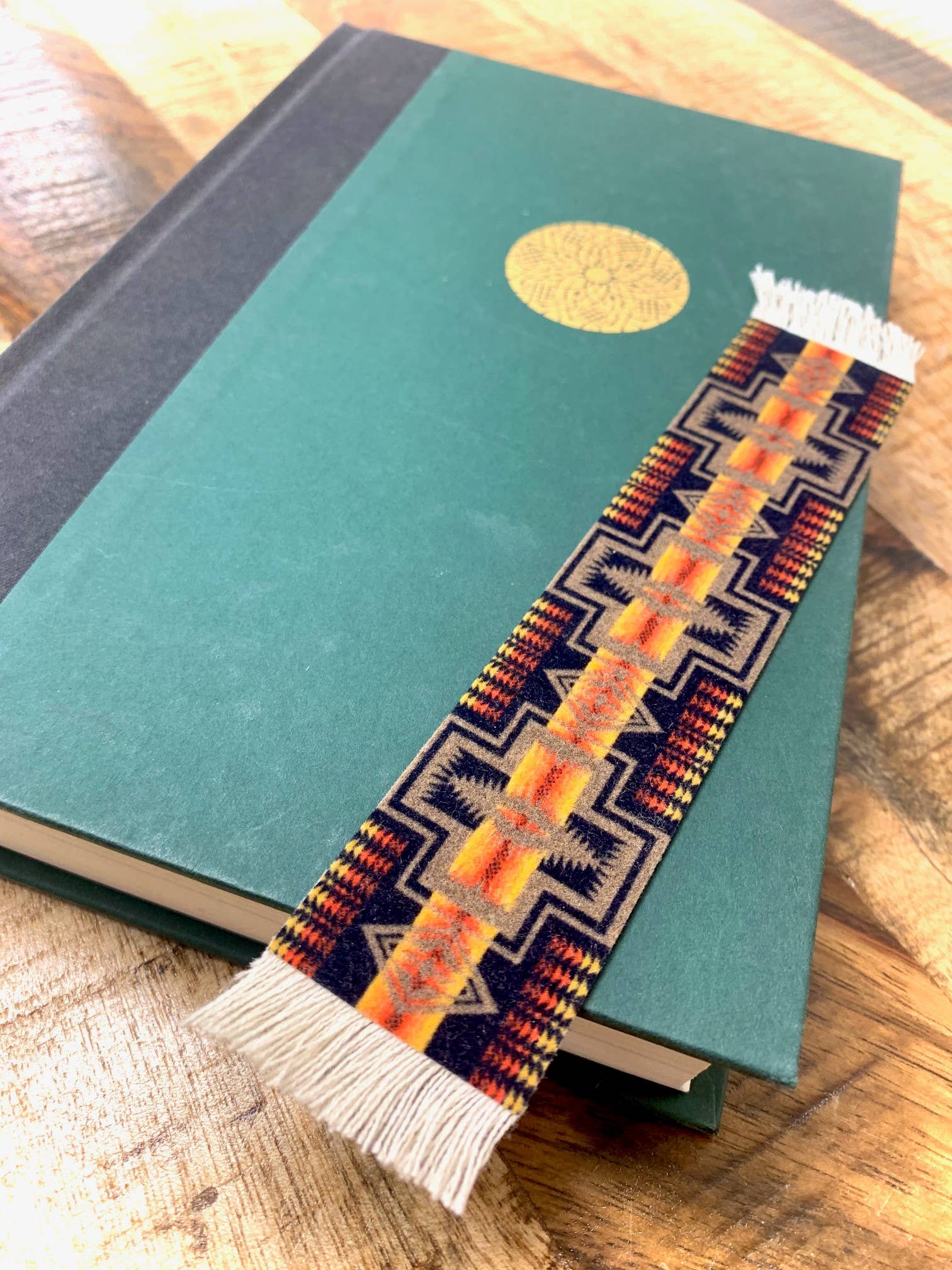 Green book with a colorful Pendleton woven bookmark on a wooden surface