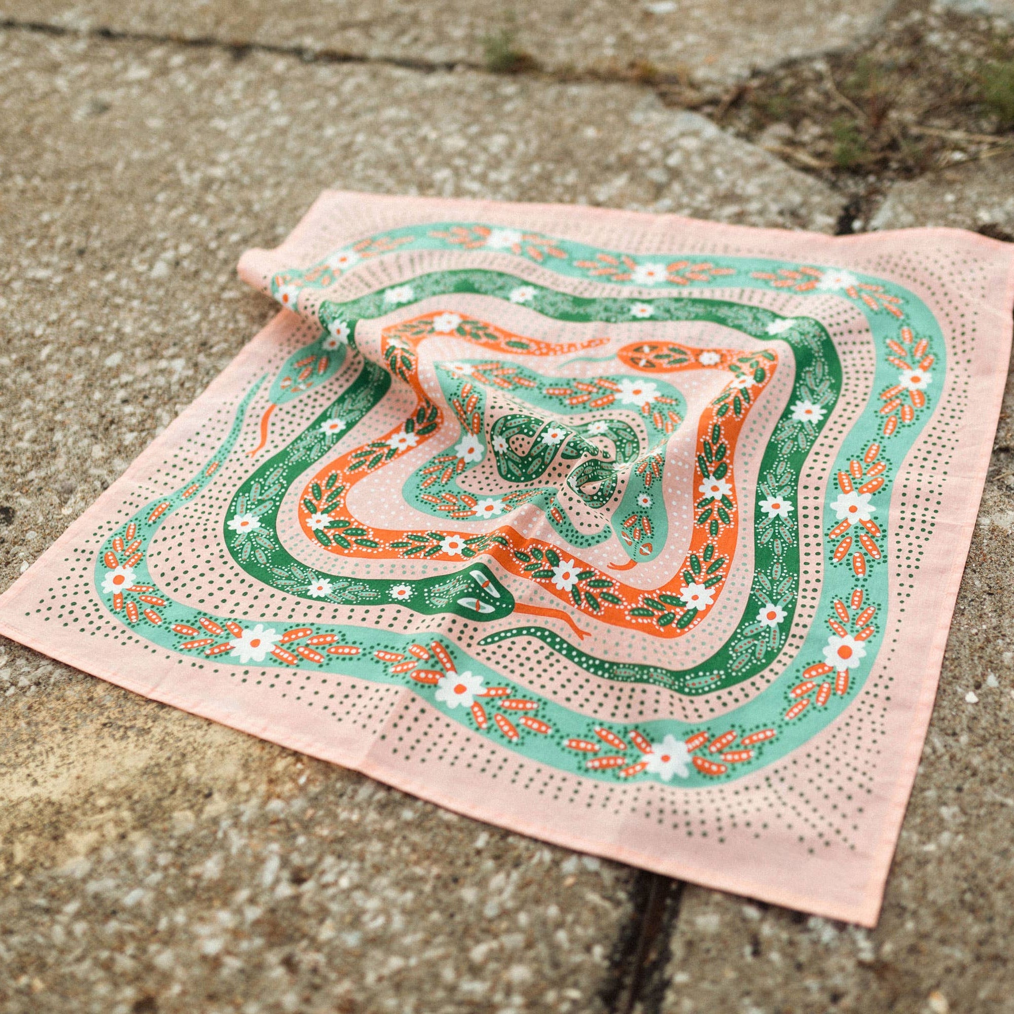Decorative bandana with green and orange snakes patterns on a concrete surface