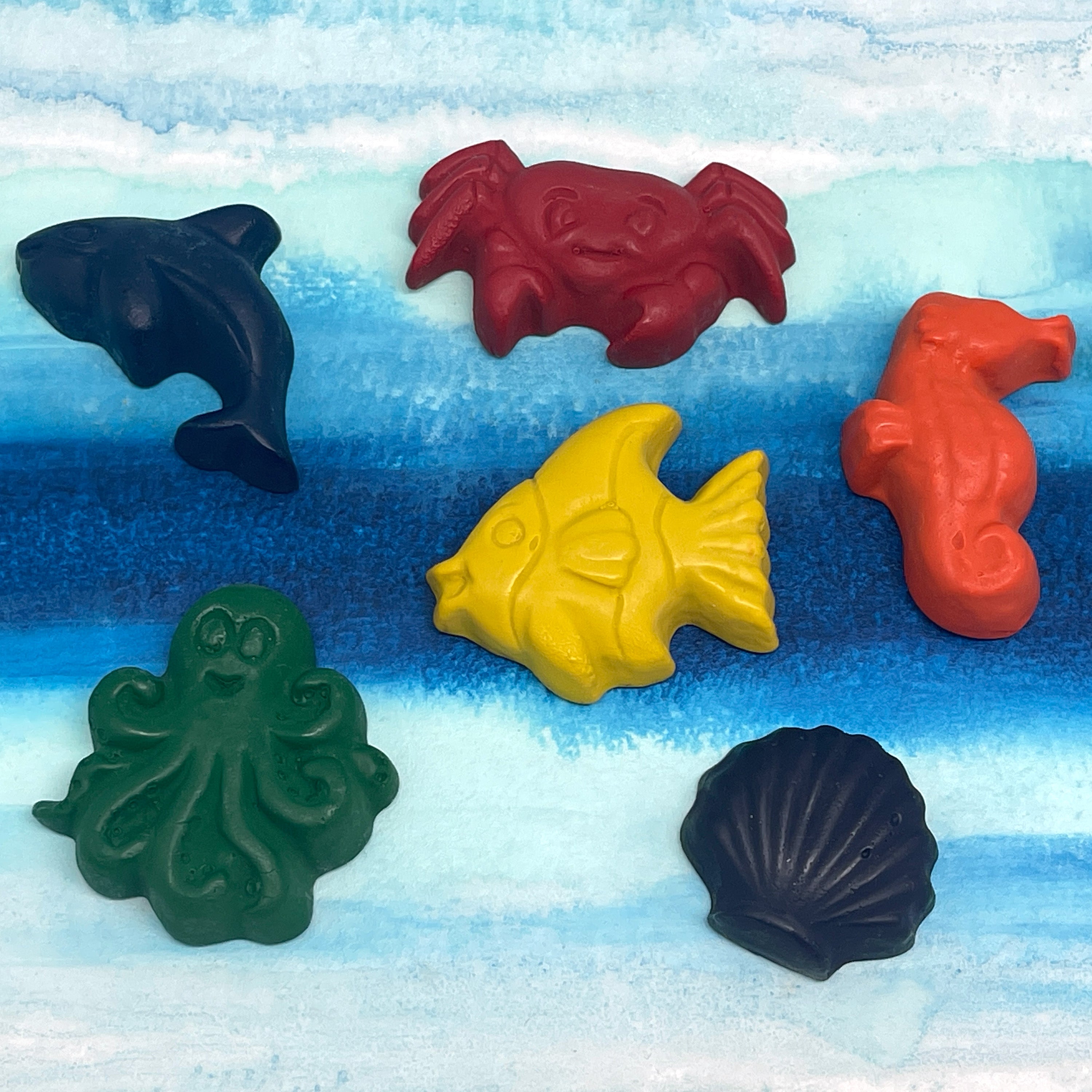 Set of colorful crayons in sea creature shapes on a blue and white striped background