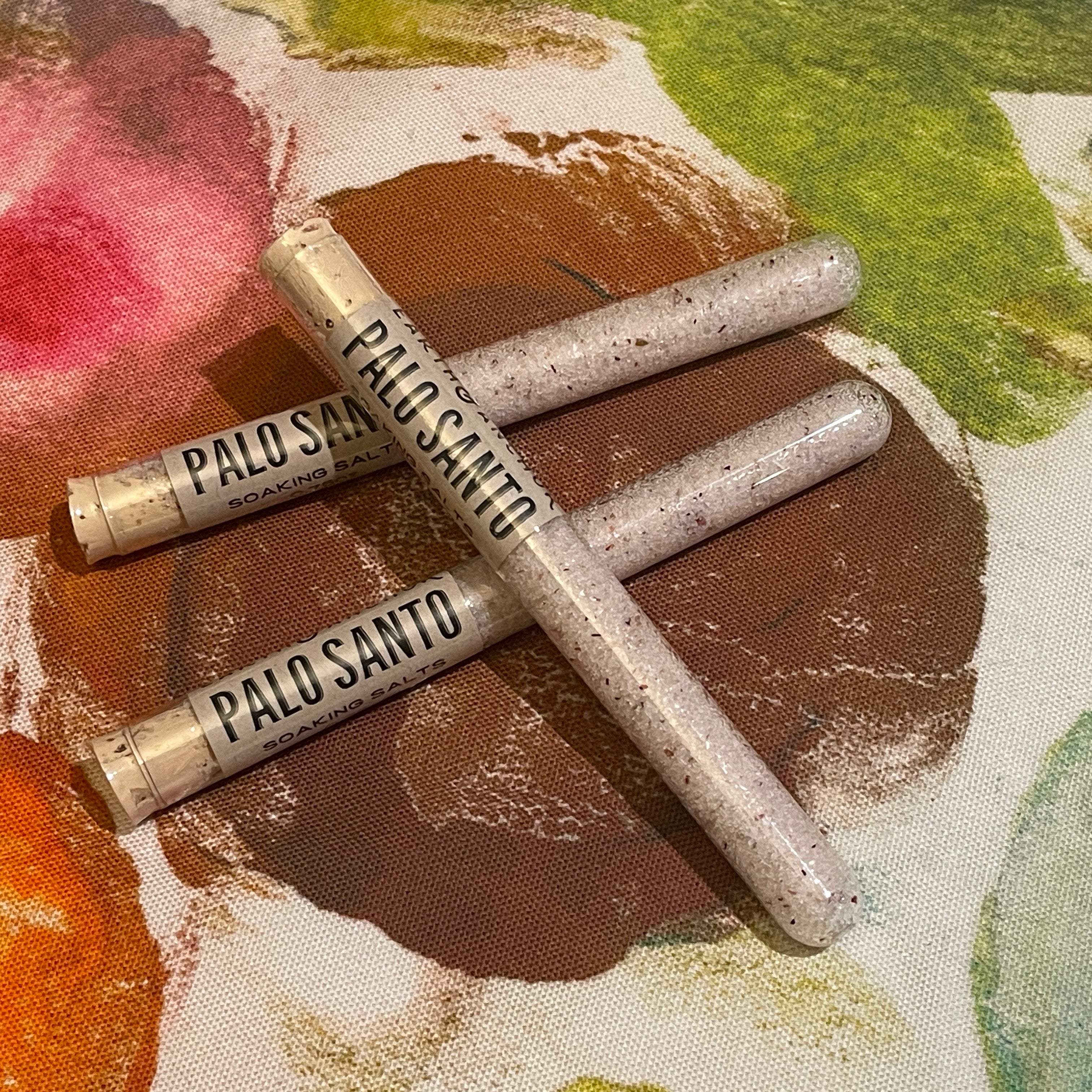 Three Palo Santo scented soaking bath salt tubes on a colorful fabric background