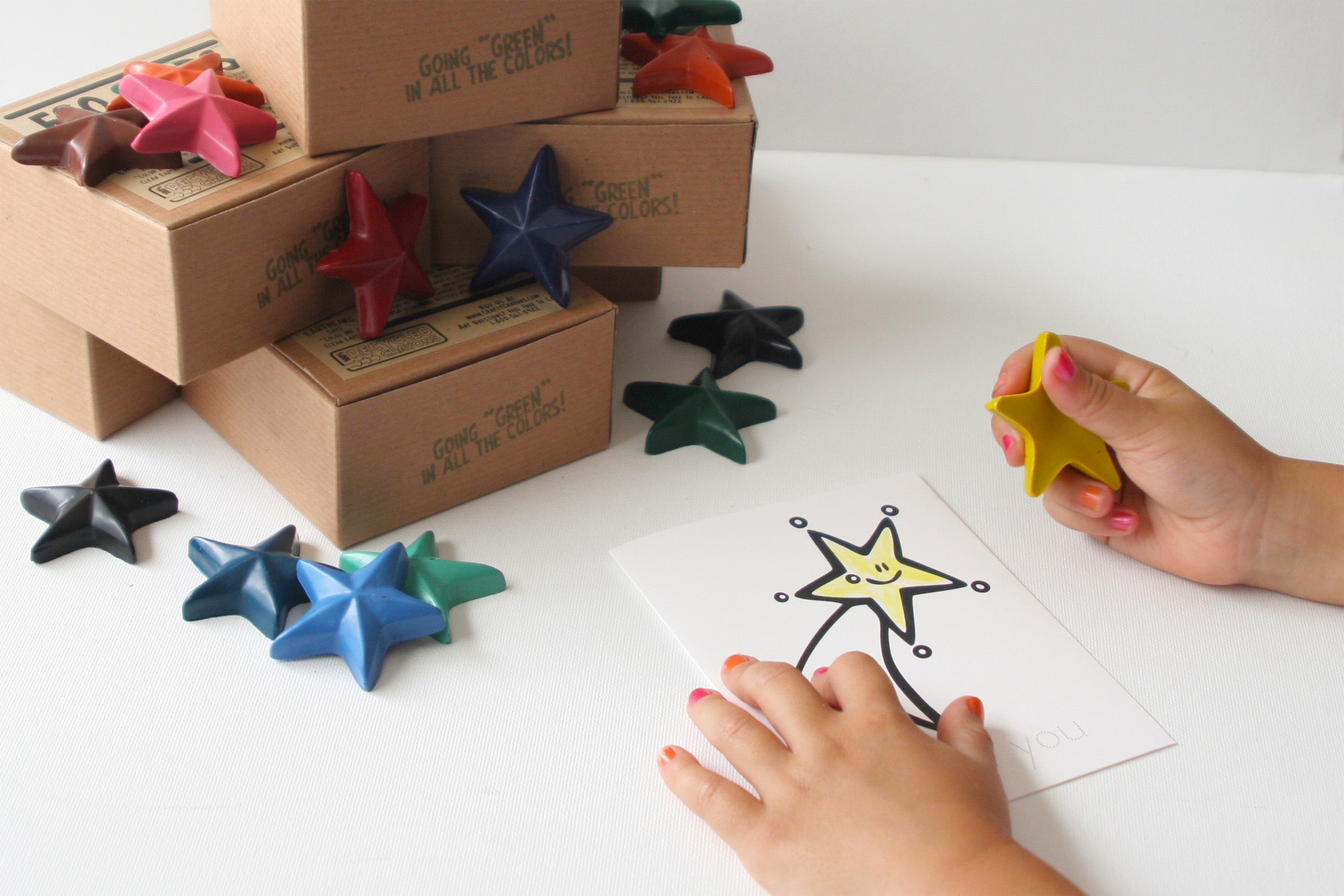 Colorful star-shaped crayons on a white surface with a child's hands interacting with them.