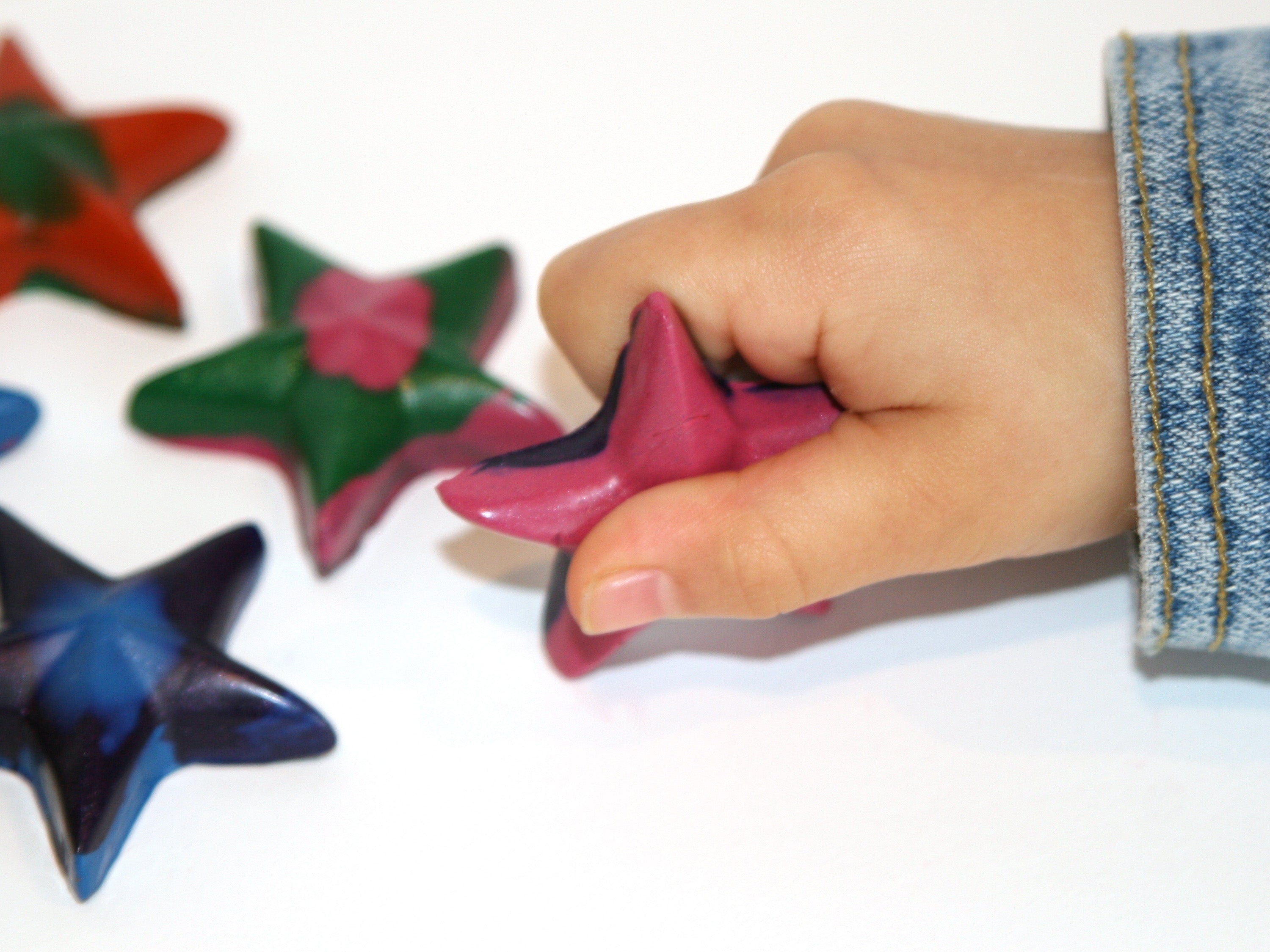 Hand holding a pink star-shaped crayon with colorful stars on a white background