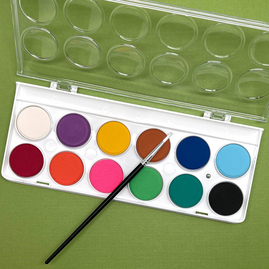 A watercolor paint palette with bright round pans of color and a paintbrush, placed on a green background.