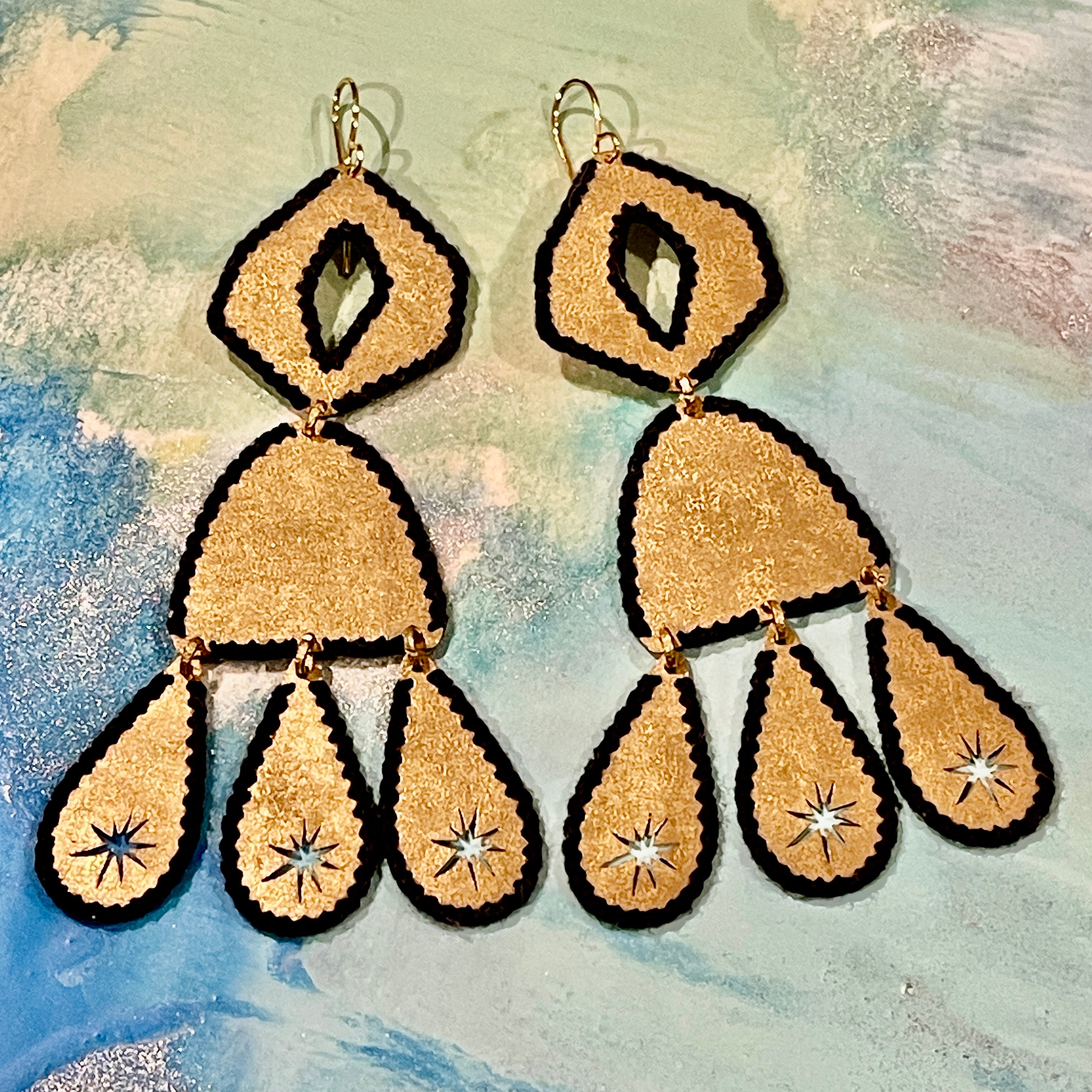 pair of gold-tone handmade brass teardrop earrings with black thread stitched edges on a muted color background