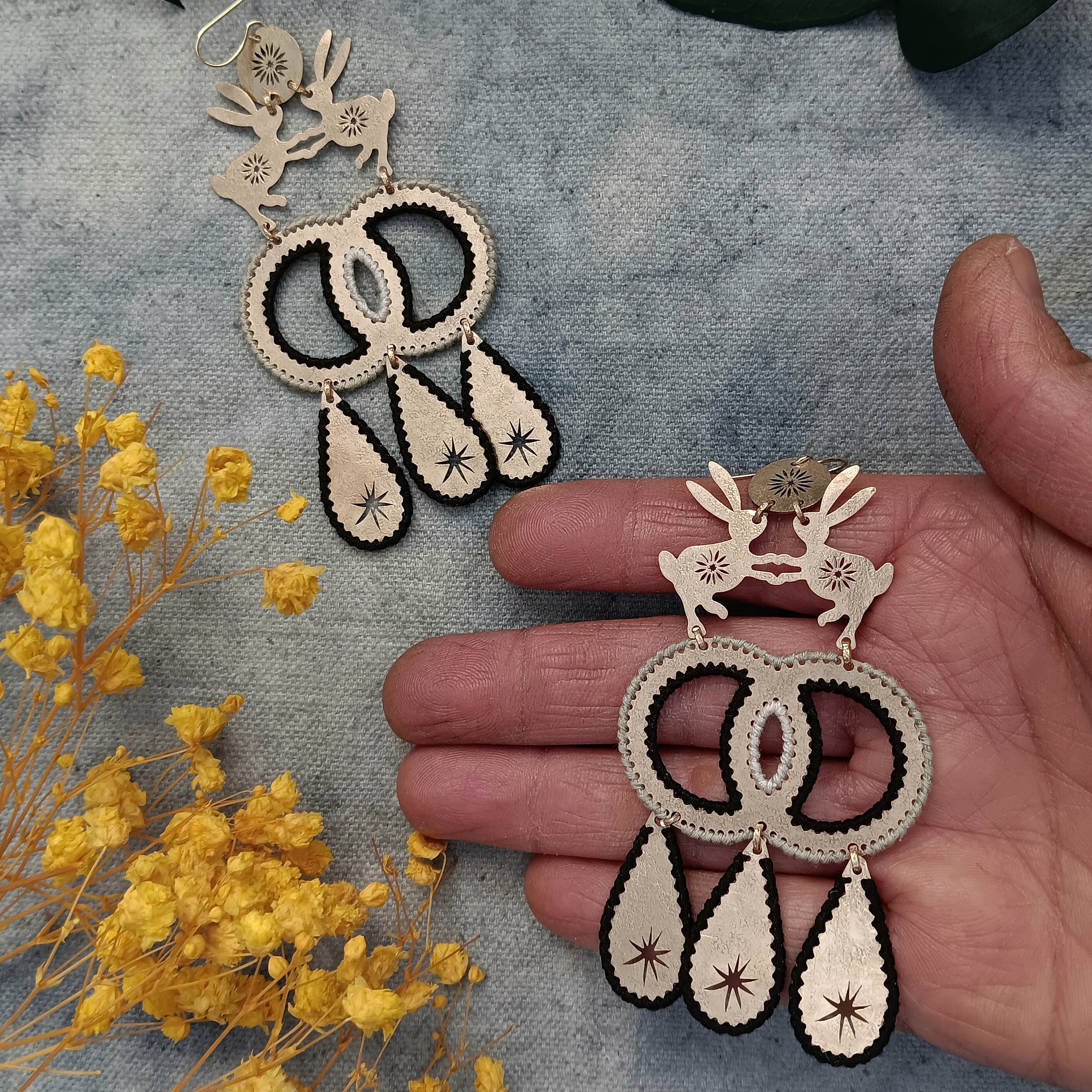 Boho earrings held by a hand with yellow flowers and green leaves in the background