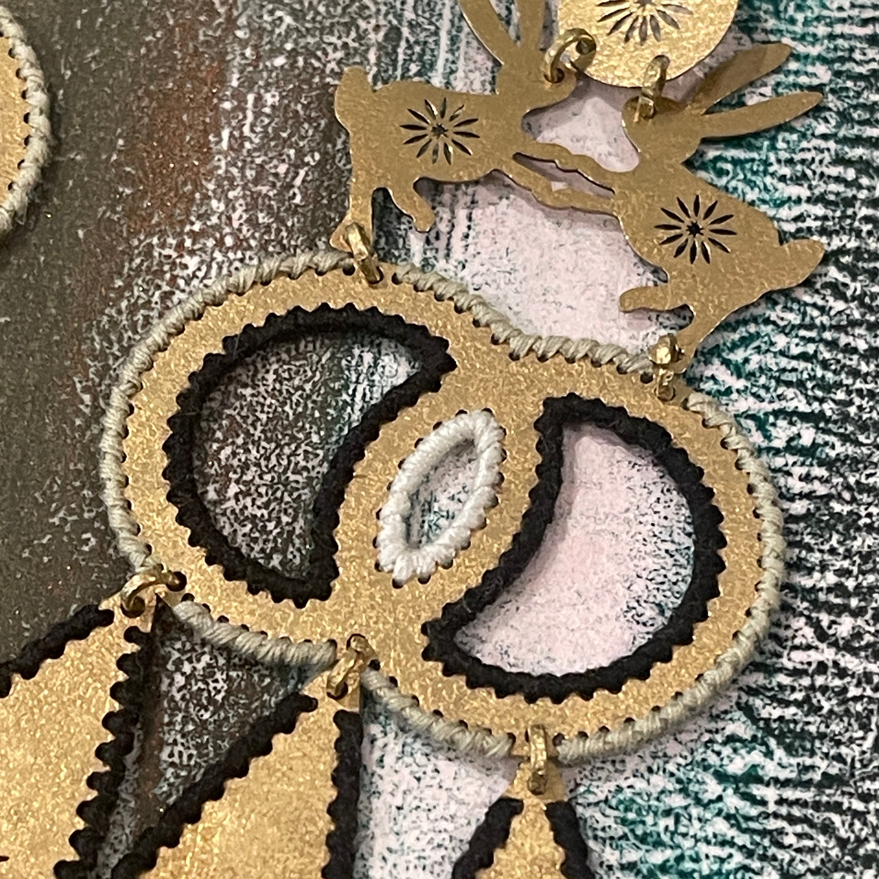Textured brass handmade earrings with two hares dancing and color thread edges on a muted background