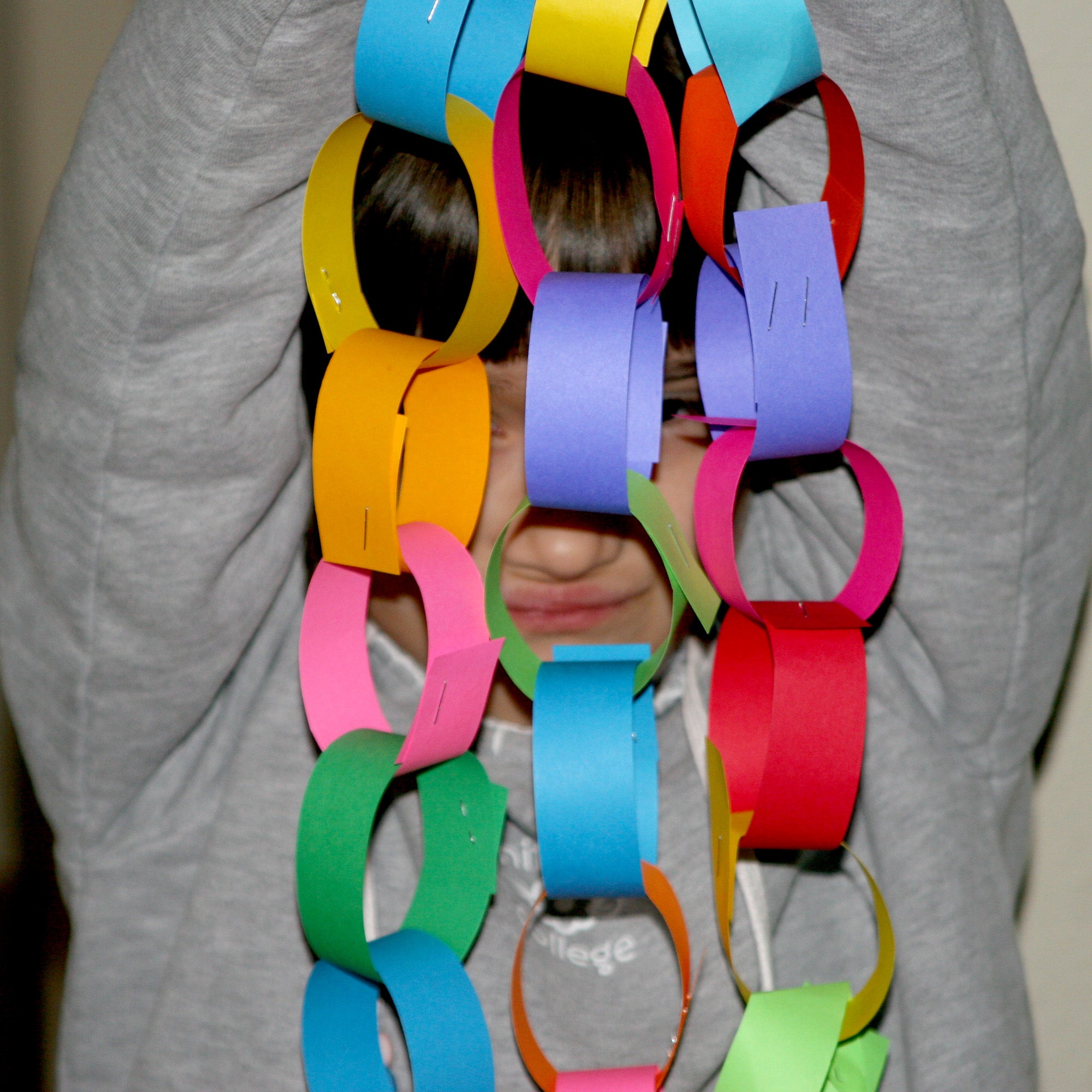 Child holding a long colorful paper chain with various colors.