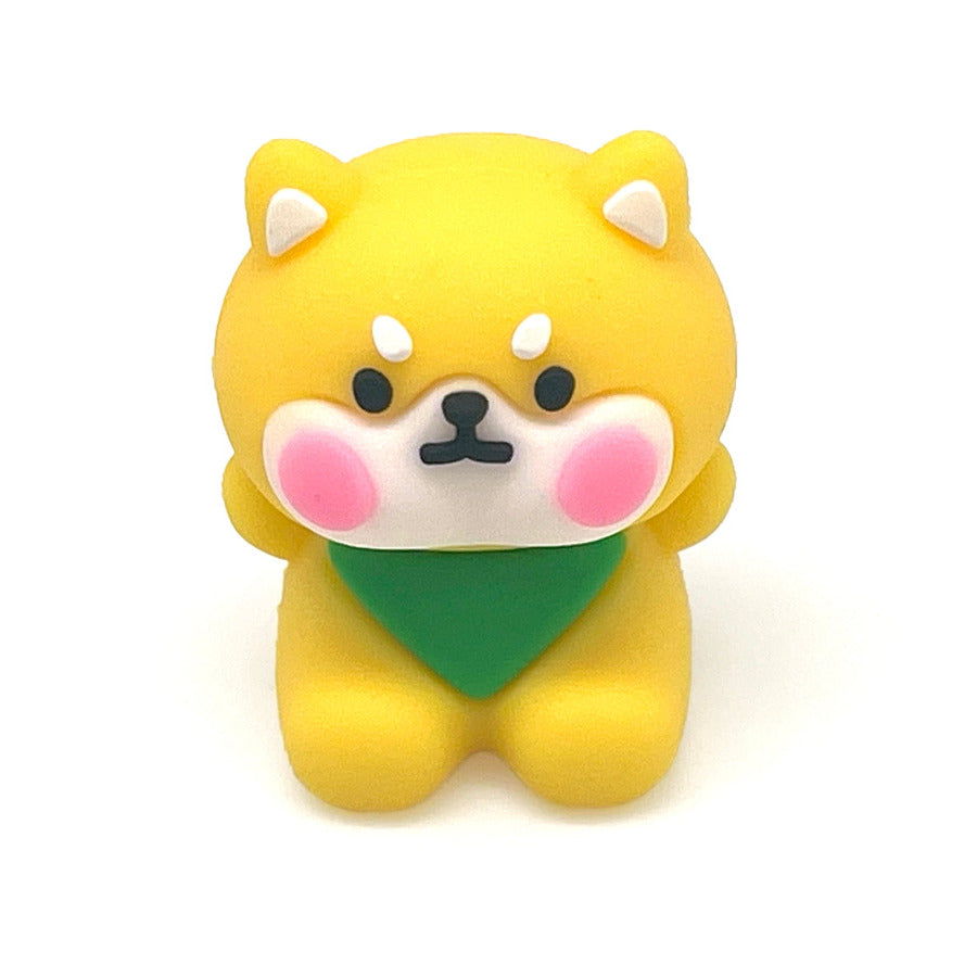A small yellow Shiba Inu dog pencil sharpener with pink cheeks, a green bandana, and a black nose, centered on a plain white background.
