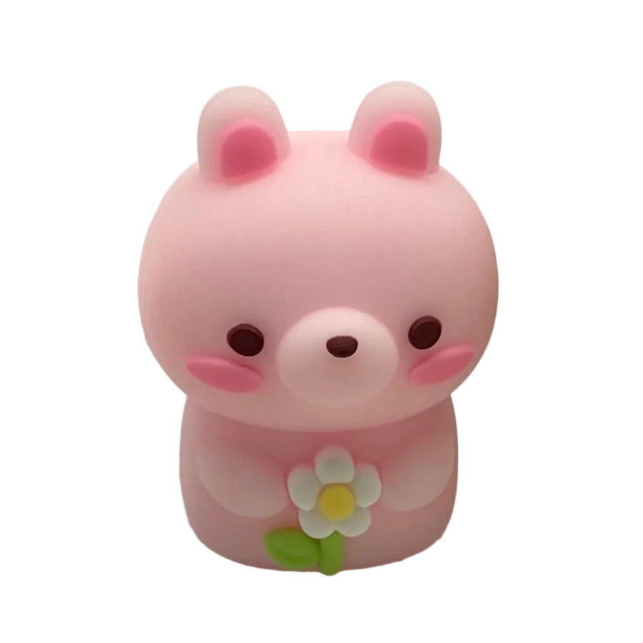 A small pink bunny shaped pencil sharpener with pink inner ears, dark brown eyes and nose, pink cheeks, and a white daisy flower with a green stem held in front of its chest, shown on a plain white background.