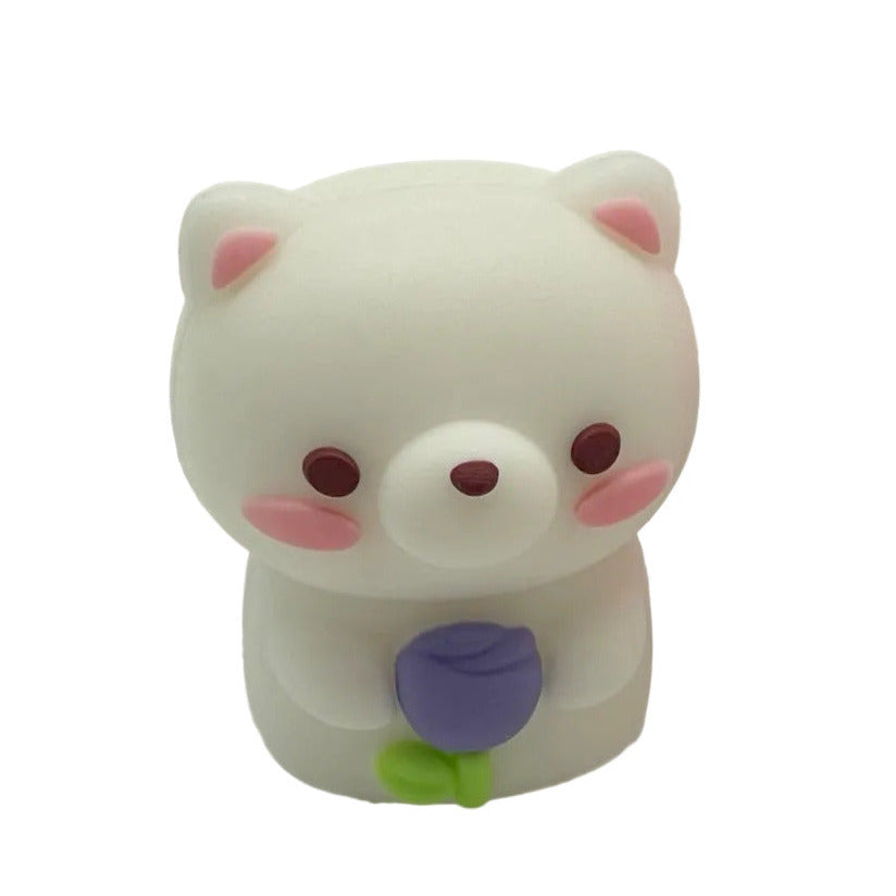 A small white bear-shaped pencil sharpener with pink inner ears, dark brown eyes and nose, pink cheeks, and a purple tulip flower with a green stem held in front of its chest, shown on a plain white background.
