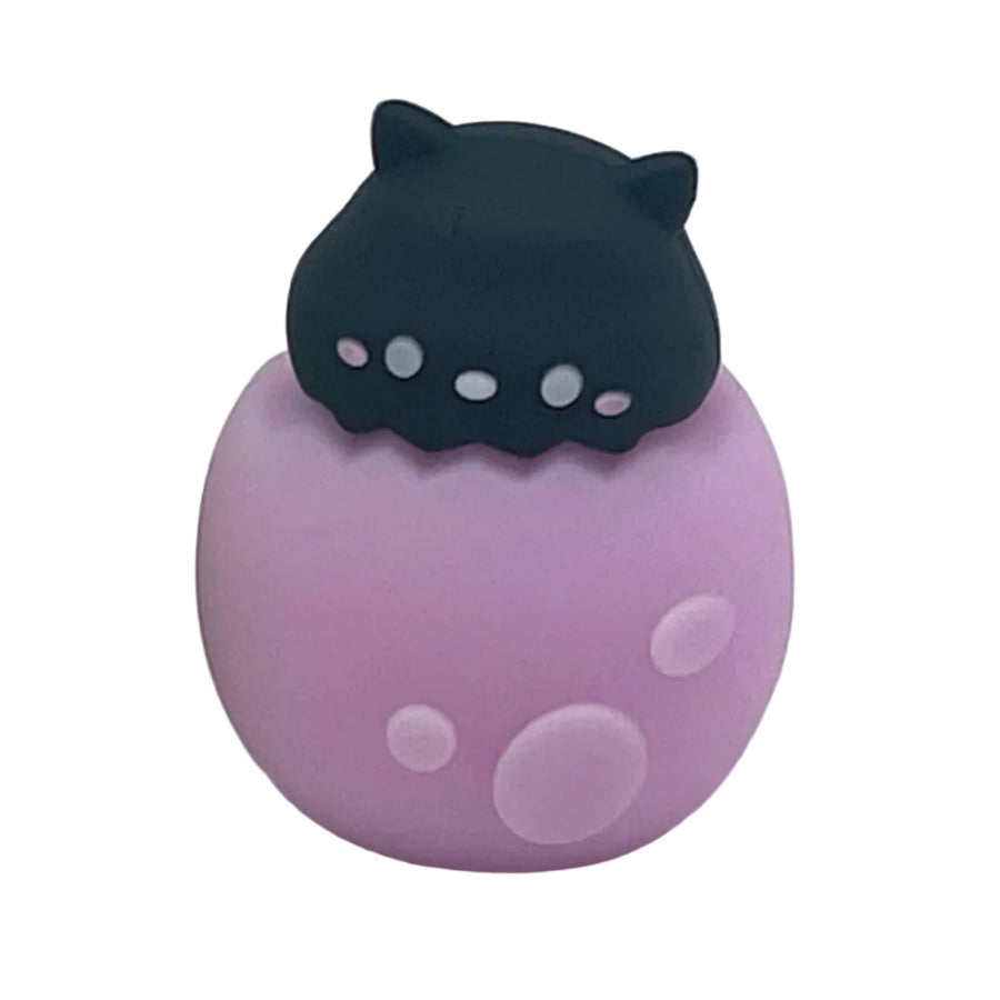 A small black cat in a purple spotted egg shape pencil sharpener with pink spots on a white background