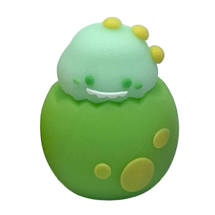 A small green dinosaur in a green spotted egg shape pencil sharpener with a light green head, yellow spots, on a white background.