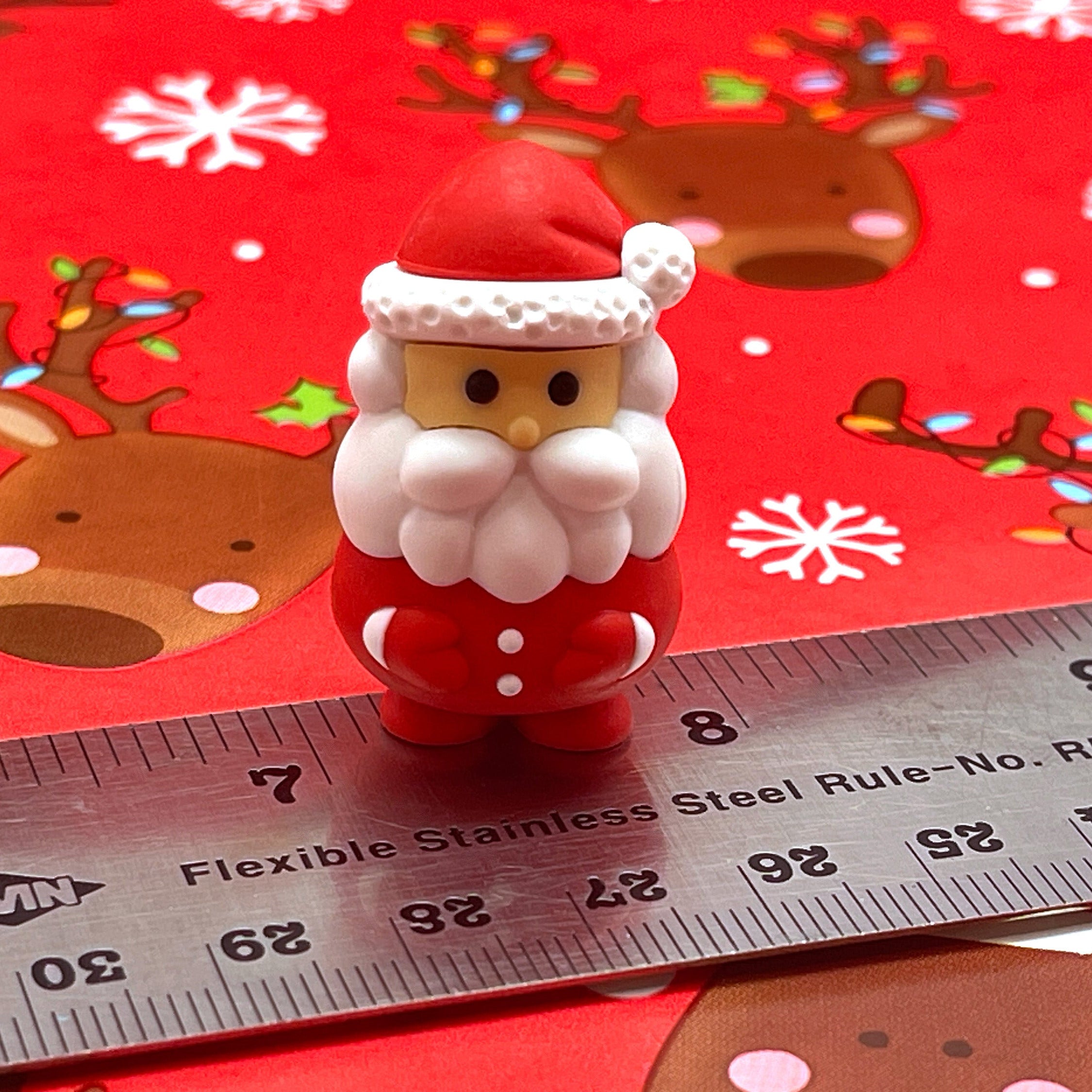 Small Santa Claus puzzle eraser on a red background with reindeer and snowflakes, next to a ruler for scale.
