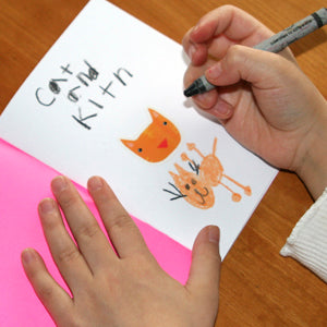 Photo of child holding a crayon and drawing a cat in a mini blank book