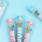Three colorful pens with pink and blue axolotl characters on a light blue background with a journal set in the corner