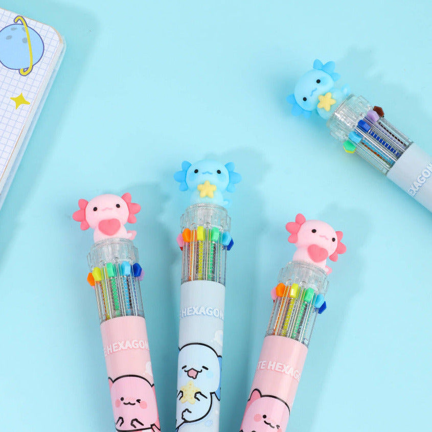 Three colorful pens with pink and blue axolotl characters on a light blue background with a journal set in the corner