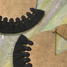Close up detail of handmade brass dangle earrings with black color thread fringe detail on a metallic painting background
