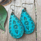 Turquoise embossed leather earrings on a wooden surface with leaves and feathers.