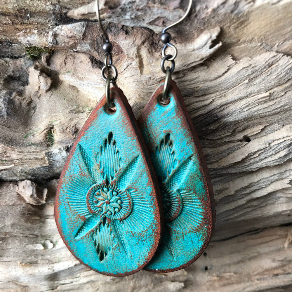 Handmade turquoise leather earrings with hand tooled western boho design on a wooden surface
