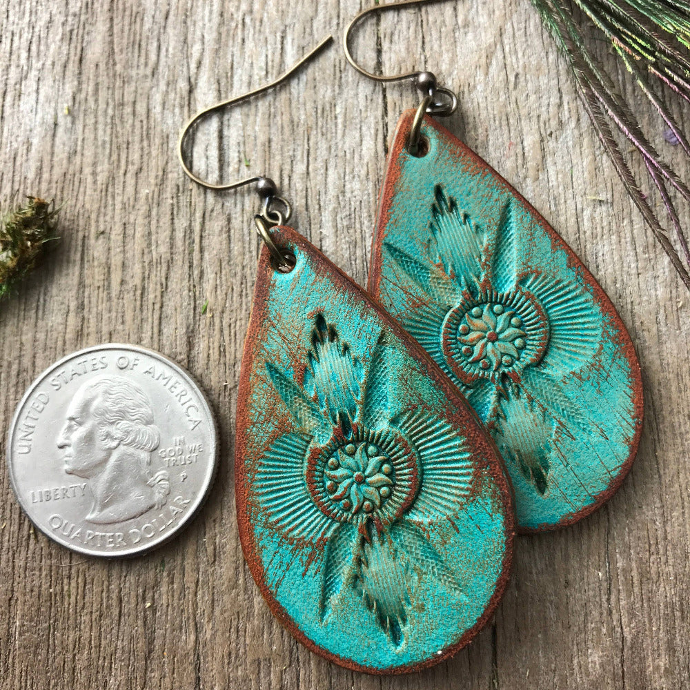 Handmade teardrop-shaped leather earrings with turquoise and brown design on a wooden surface with a coin for scale. Made in USA