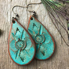 Turquoise leather dangle earrings with embossed designs on a wooden surface with peacock feathers.