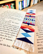 Colorful geometric Pendleton Blanket patterned bookmark on an open book with blurred bookshelf in the background