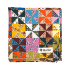 A folded square bandana featuring a colorful patchwork calico design with geometric and floral patterns, including orange, pink, blue, yellow, green, and brown. A white fabric label reading Handker is sewn onto the lower right area.