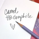 Purple Camel HB graphite pencil on a white sheet of paper with 'Camel HB Graphite' hand writing text and a heart.