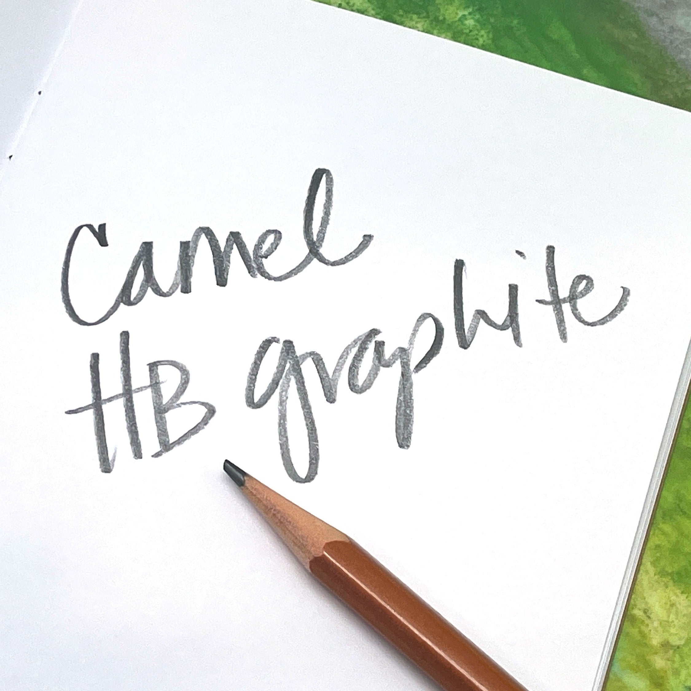 Notebook with 'Camel HB graphite' text and a pencil on a green surface