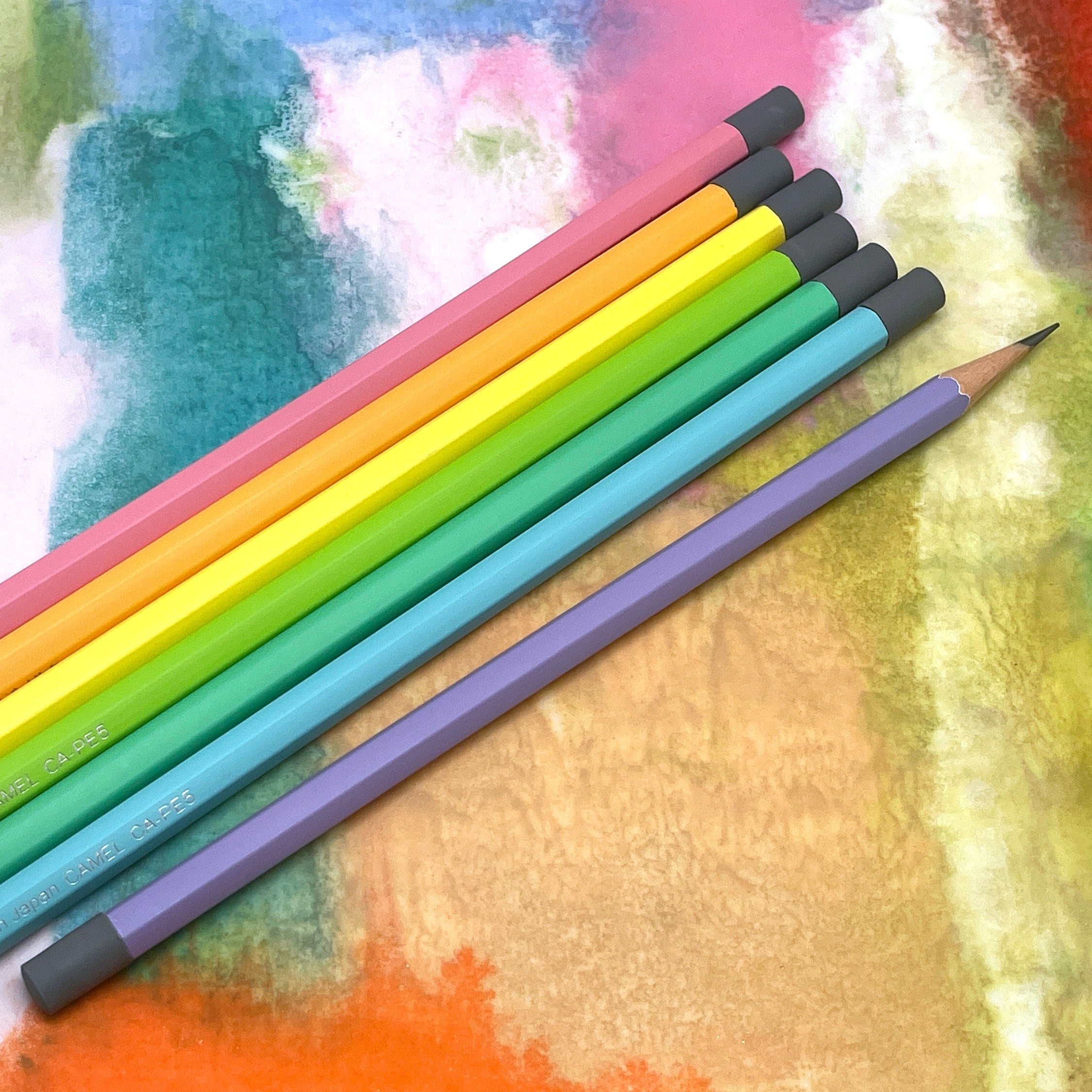 Set of colorful Camel graphite pencils on a textured surface with watercolor-like background