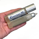 Adult hand holding 2 tubes of Coccoina liquid glue against a white background